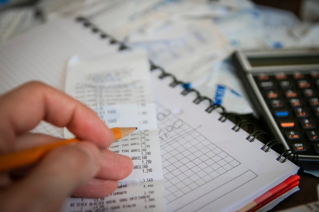 A receipt being added up by hand beside a calculator